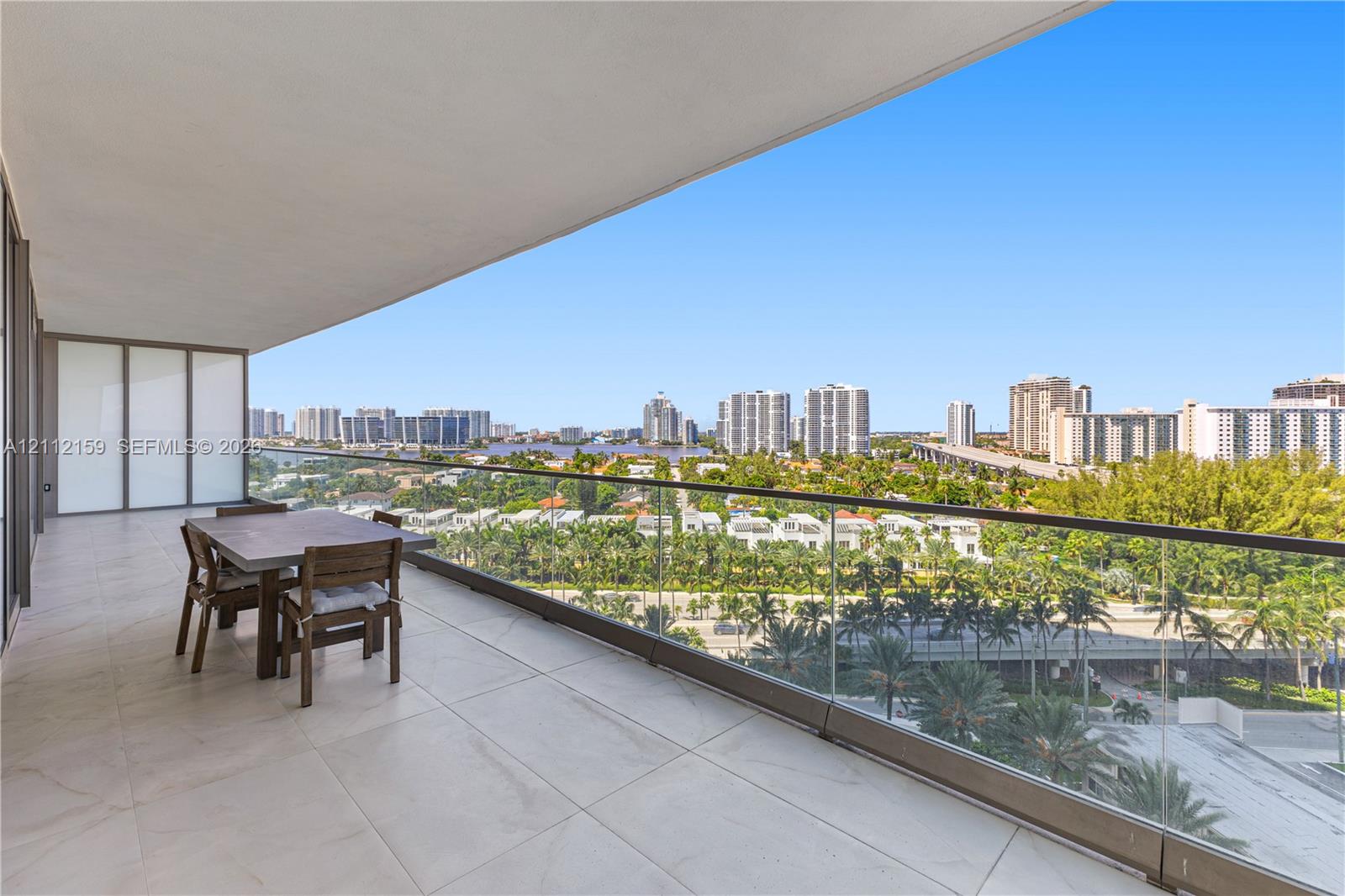 Expansive covered balcony featuring large-format stone tile flooring and a sleek frameless glass railing