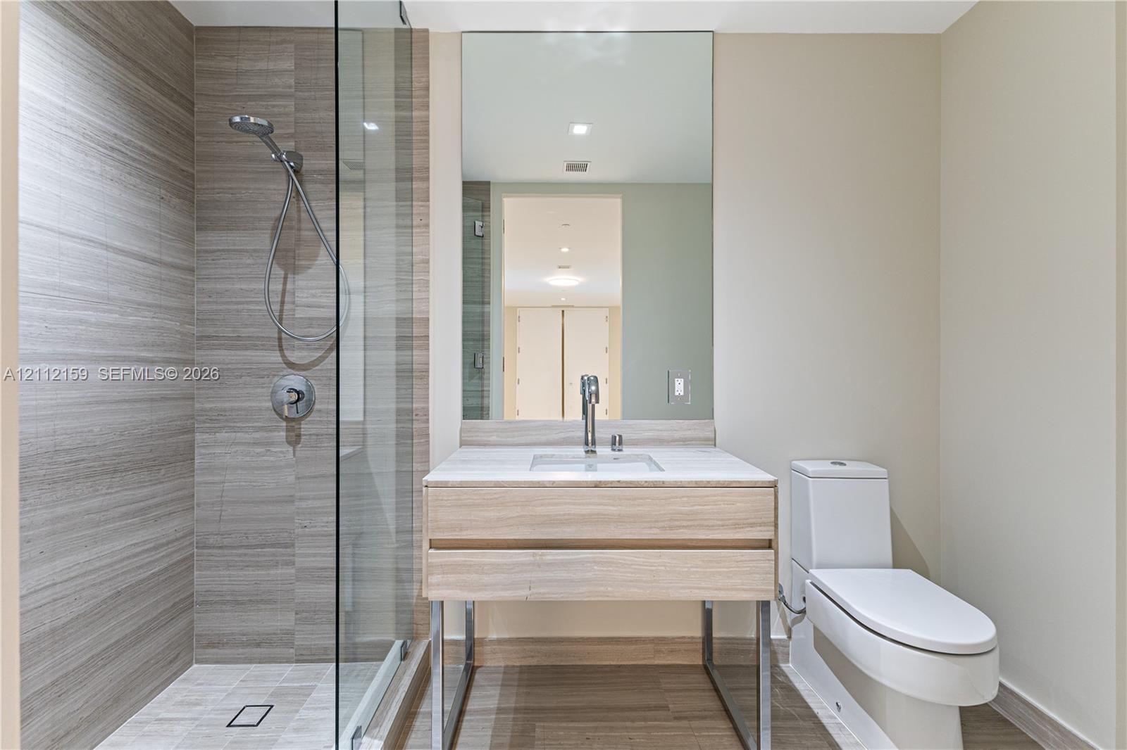 Modern bathroom featuring a wood-finish floating vanity with a light stone countertop, a glass-enclosed shower with horizontal-patterned wall tile, and a wall-to-wall vanity mirror
