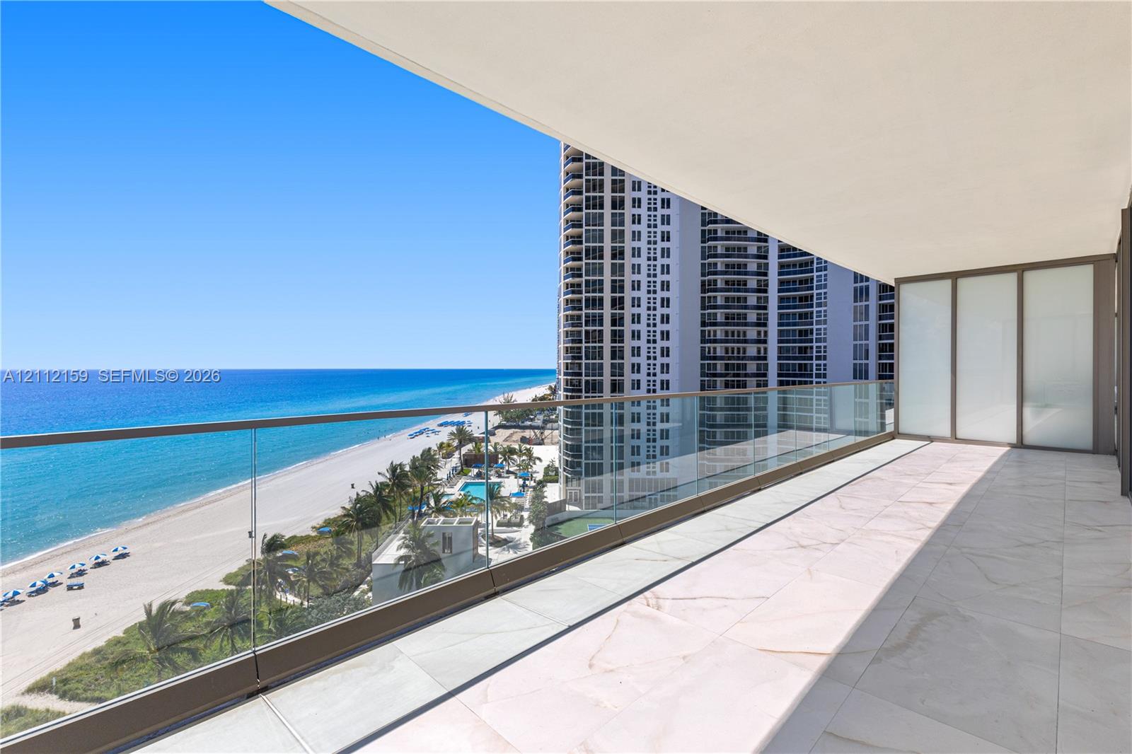Private balcony featuring light-toned tile flooring, a glass panel railing, and a covered ceiling