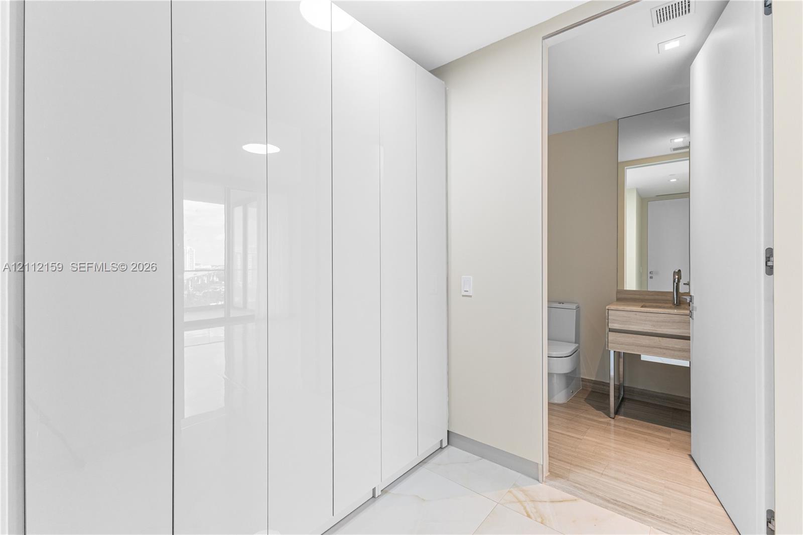 Floor-to-ceiling high-gloss white built-in cabinetry, large-format tile flooring, vanity with wood-finish cabinetry, rectangular vessel sink, and wall-mounted faucet