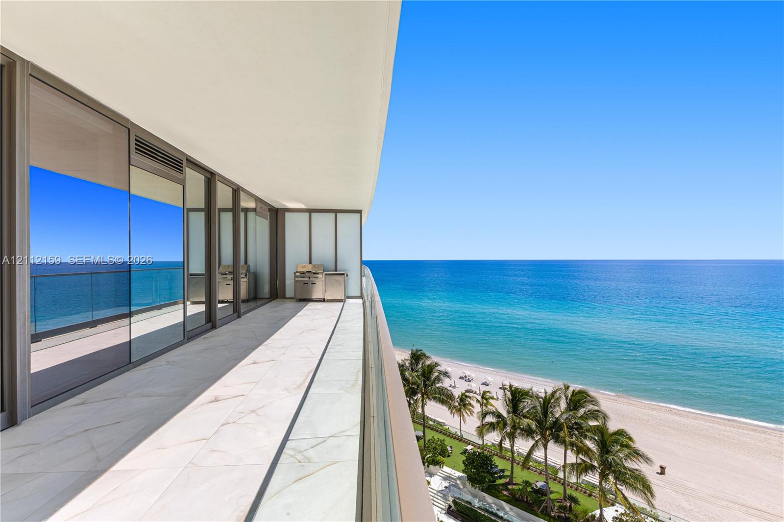 Expansive balcony featuring large-format tile flooring, a glass panel railing, built-in stainless steel outdoor kitchen equipment, and full-height sliding glass doors