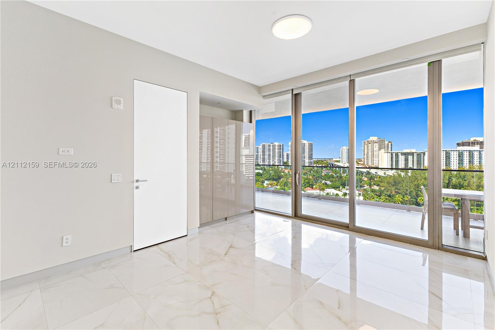 Interior space featuring large-format stone-look porcelain tile flooring, floor-to-ceiling glass sliding doors, built-in high-gloss cabinetry, and a covered balcony