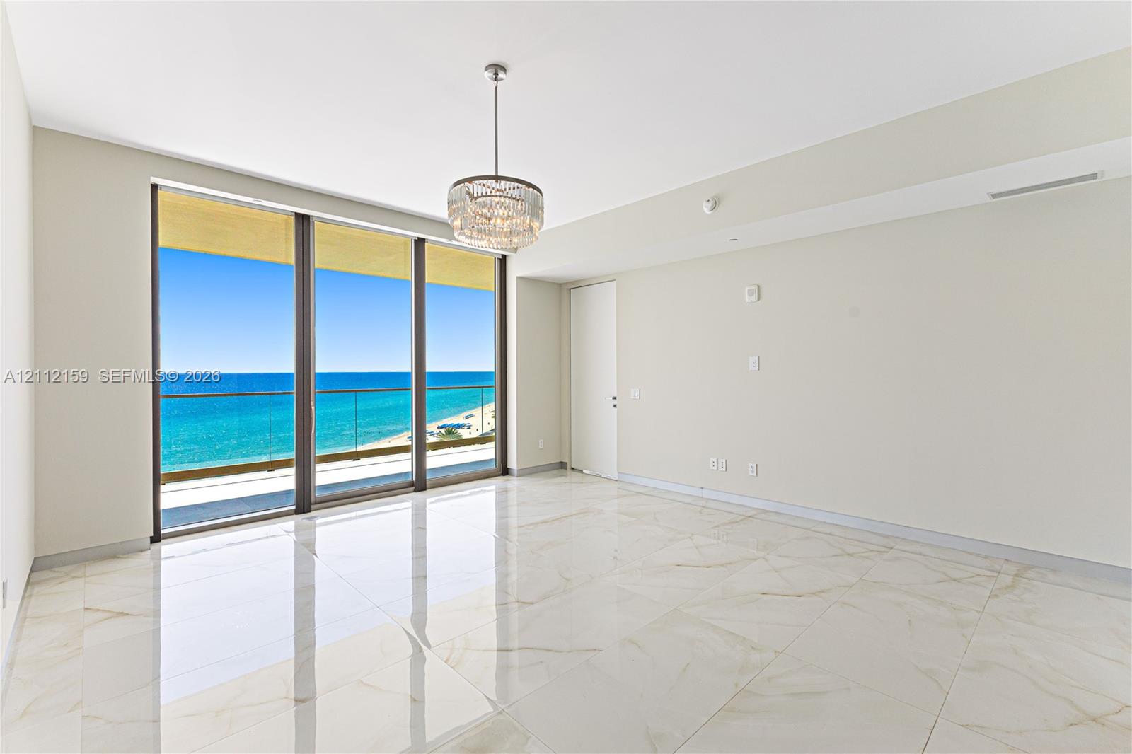 Large-format tile flooring with polished finish, floor-to-ceiling sliding glass doors, private balcony, and decorative multi-tiered crystal chandelier