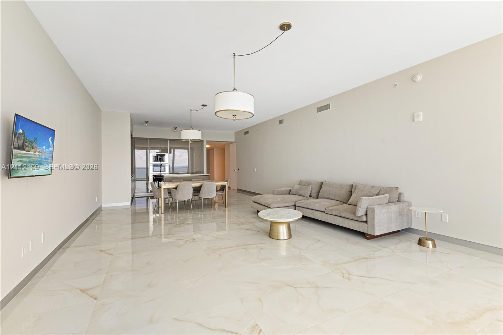 Open-concept interior featuring polished large-format stone flooring, neutral wall finishes, and dual drum-style pendant light fixtures