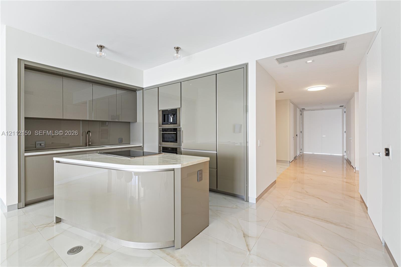 Kitchen featuring high-gloss cabinetry, stone-surface center island with integrated cooktop, built-in double wall oven, and large-format tile flooring Kitchen featuring high-gloss cabinetry, stone-surface center island with integrated cooktop, built-in double wall oven, and large-format tile flooring