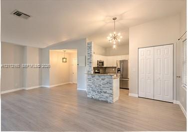 Interior featuring wood-finish flooring, stone-veneer accent half-wall, vaulted ceiling, multi-light chandelier, and floor-to-ceiling bi-fold closet doors