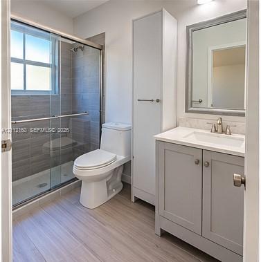 Bathroom featuring a vanity with a light-colored countertop, integrated tall cabinetry, a glass-enclosed shower with horizontal tile surround, and wood-finish flooring Bathroom featuring a vanity with a light-colored countertop, integrated tall cabinetry, a glass-enclosed shower with horizontal tile surround, and wood-finish flooring