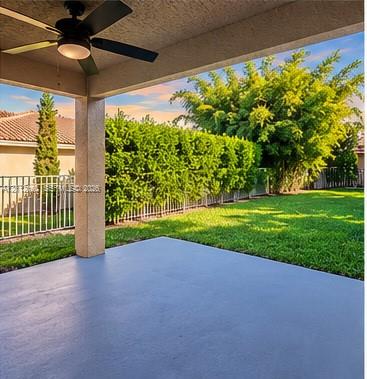 Covered patio featuring a ceiling fan, concrete flooring, manicured lawn, metal fencing, and perimeter hedging Covered patio featuring a ceiling fan, concrete flooring, manicured lawn, metal fencing, and perimeter hedging