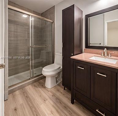 Bathroom featuring a dark wood-finish vanity with an integrated storage tower, wood-finish flooring, and a glass-enclosed shower with horizontal tile surround Bathroom featuring a dark wood-finish vanity with an integrated storage tower, wood-finish flooring, and a glass-enclosed shower with horizontal tile surround