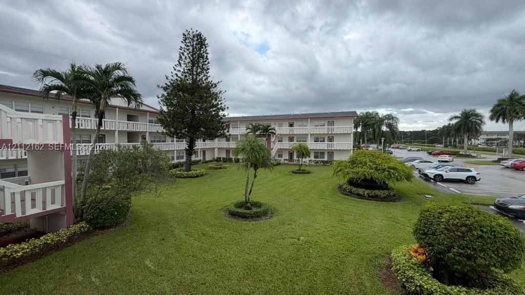 Multi-level building exterior featuring white railings, expansive manicured lawn, mature palm trees, and structural balcony walkways