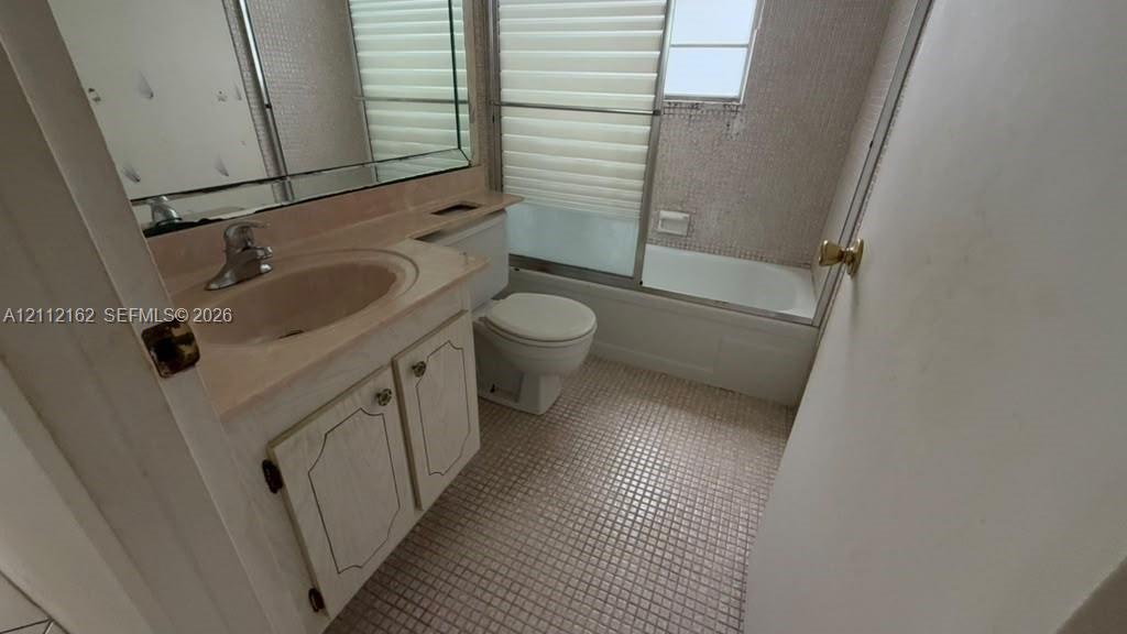 Bathroom featuring a vanity with integrated sink, large wall-mounted mirror, mosaic tile flooring, and a bathtub with sliding glass doors