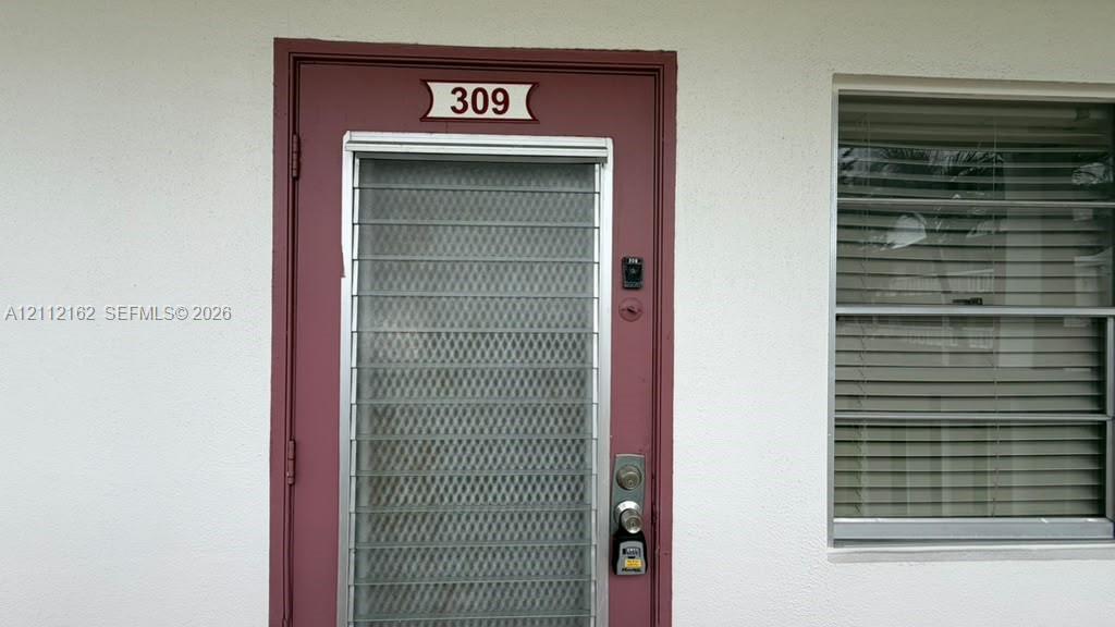 Entrance featuring a maroon door with a full-length screen and horizontal blinds, paired with a matching window