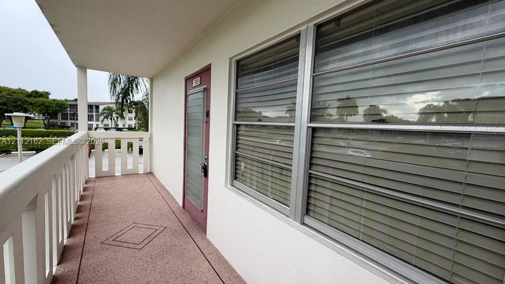 Covered exterior corridor with concrete flooring, white protective railing, and exterior entrance door