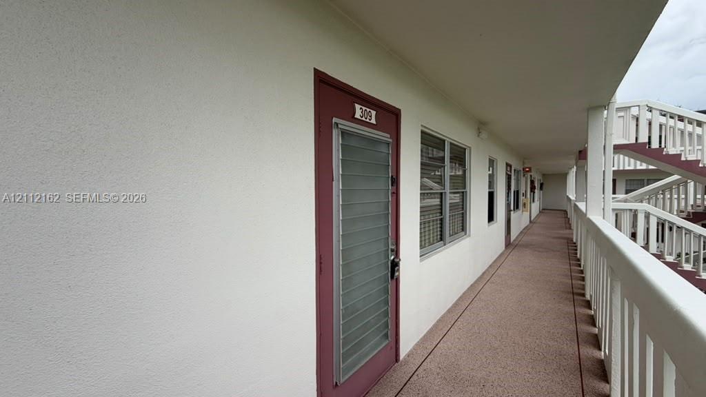 Exterior corridor featuring stucco wall finishes, metal louvered storm doors, multi-pane windows, and a covered balcony with a white railing system