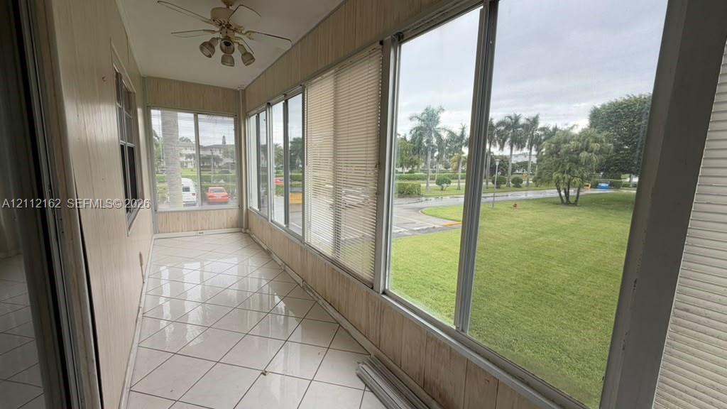 Enclosed sunroom featuring expansive glass windows, ceramic tile flooring, vertical wood-panel wall finish, and a ceiling-mounted light fixture