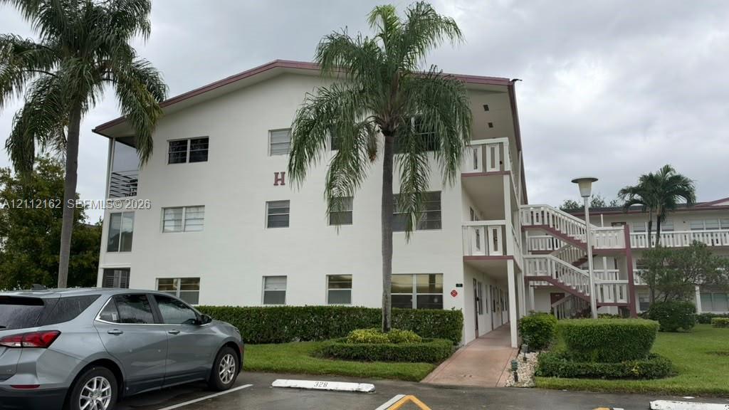 Three-story building exterior featuring smooth stucco siding, railed balcony access, open-air staircase, and integrated landscaping