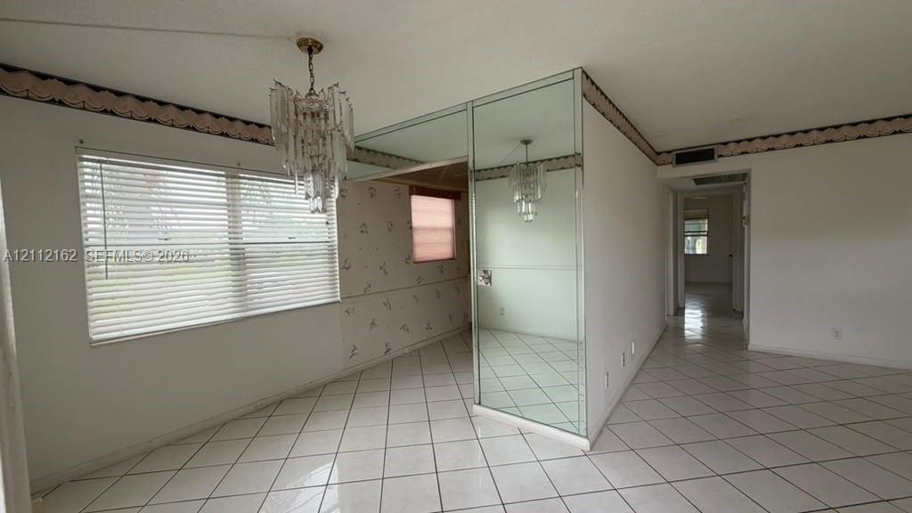 Interior space featuring white tile flooring, floor-to-ceiling mirrored wall cladding, and a multi-tiered crystal chandelier Interior space featuring white tile flooring, floor-to-ceiling mirrored wall cladding, and a multi-tiered crystal chandelier