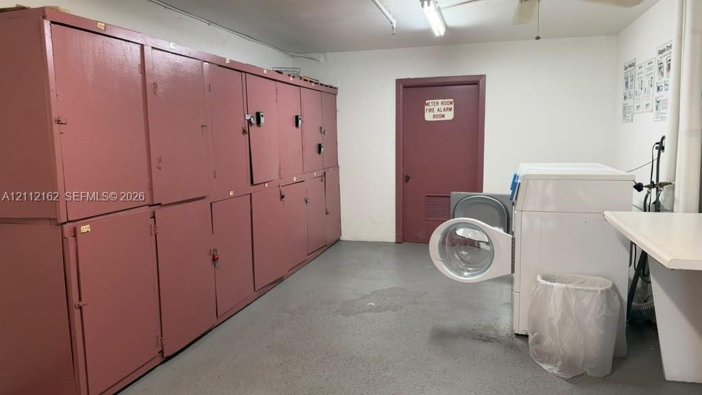 Utility room featuring an integrated wall of metal storage lockers, concrete flooring, and ceiling-mounted lighting