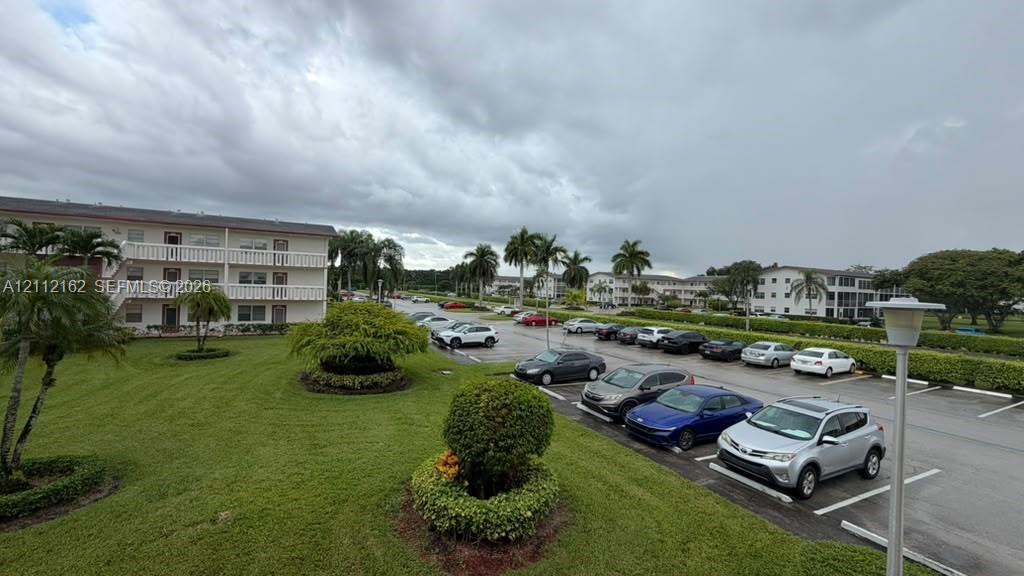 Exterior of a multi-story building featuring stucco siding, assigned surface parking, manicured landscaping, and mature palm trees