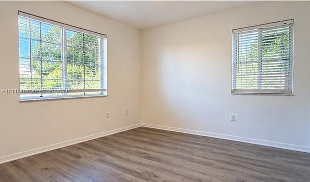 Neutral interior space featuring wood-finish flooring, dual windows, and fitted horizontal blinds