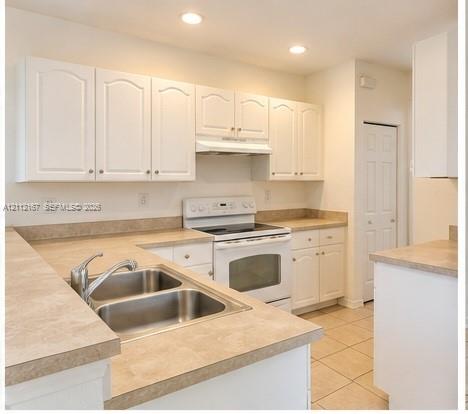 Kitchen featuring white cabinetry, integrated range, dual-basin stainless steel sink with high-arc faucet, neutral laminate countertops, and tile flooring