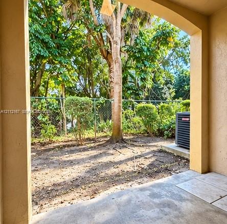 Covered patio featuring concrete flooring, an arched entryway, chain-link perimeter fencing, and mature landscape