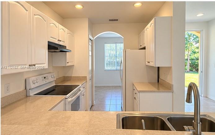 Kitchen featuring white cabinetry, solid-surface countertops, dual-basin stainless steel sink with gooseneck faucet, and recessed lighting