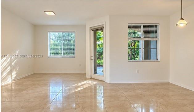 Open interior space featuring light-toned tile flooring, neutral wall paint, two dual-pane windows with horizontal blinds, and a glass-paneled exterior door