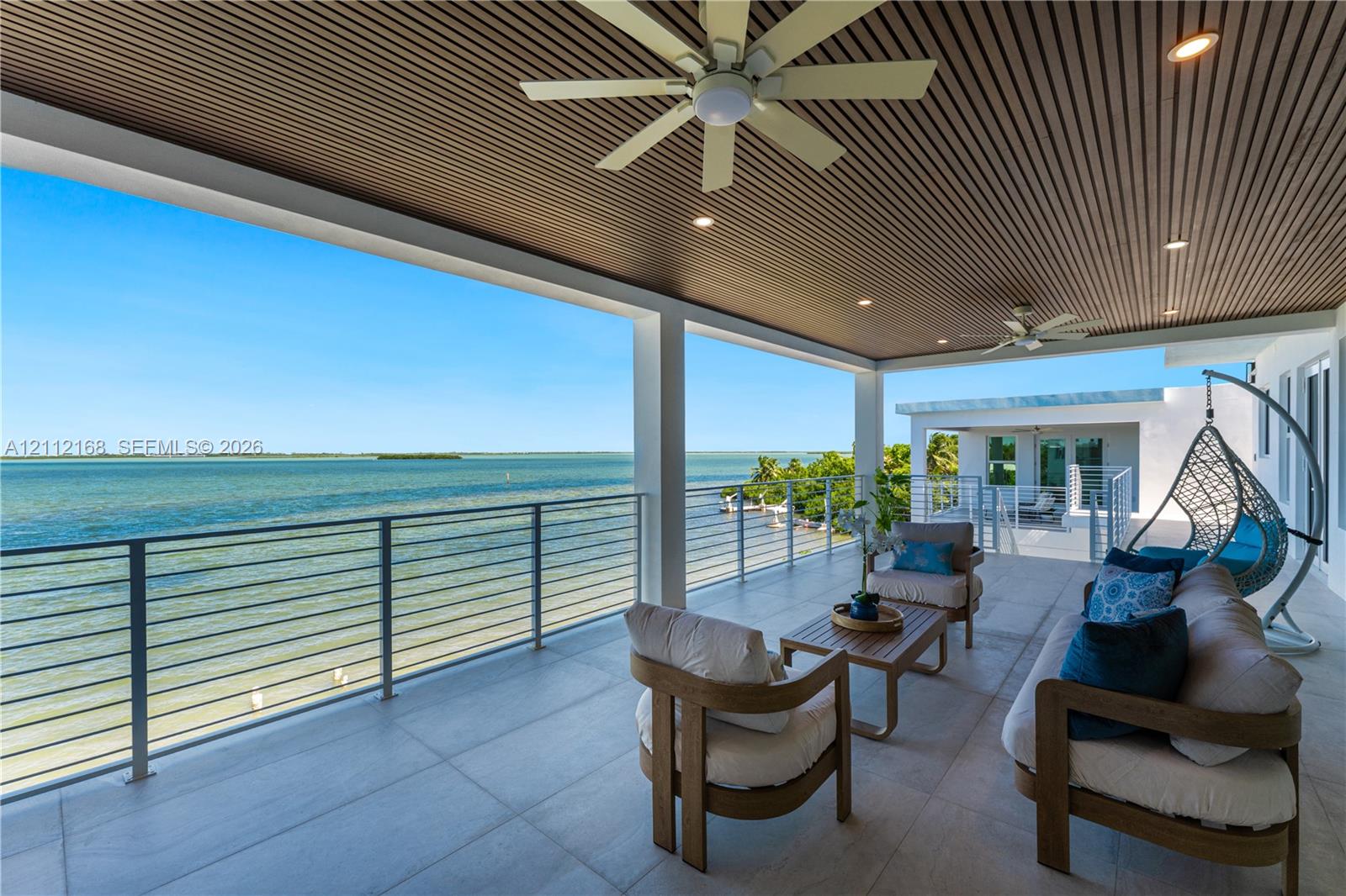 Covered terrace featuring a slatted wood ceiling, recessed lighting, ceiling fans, large-format tile flooring, and a stainless steel cable railing system