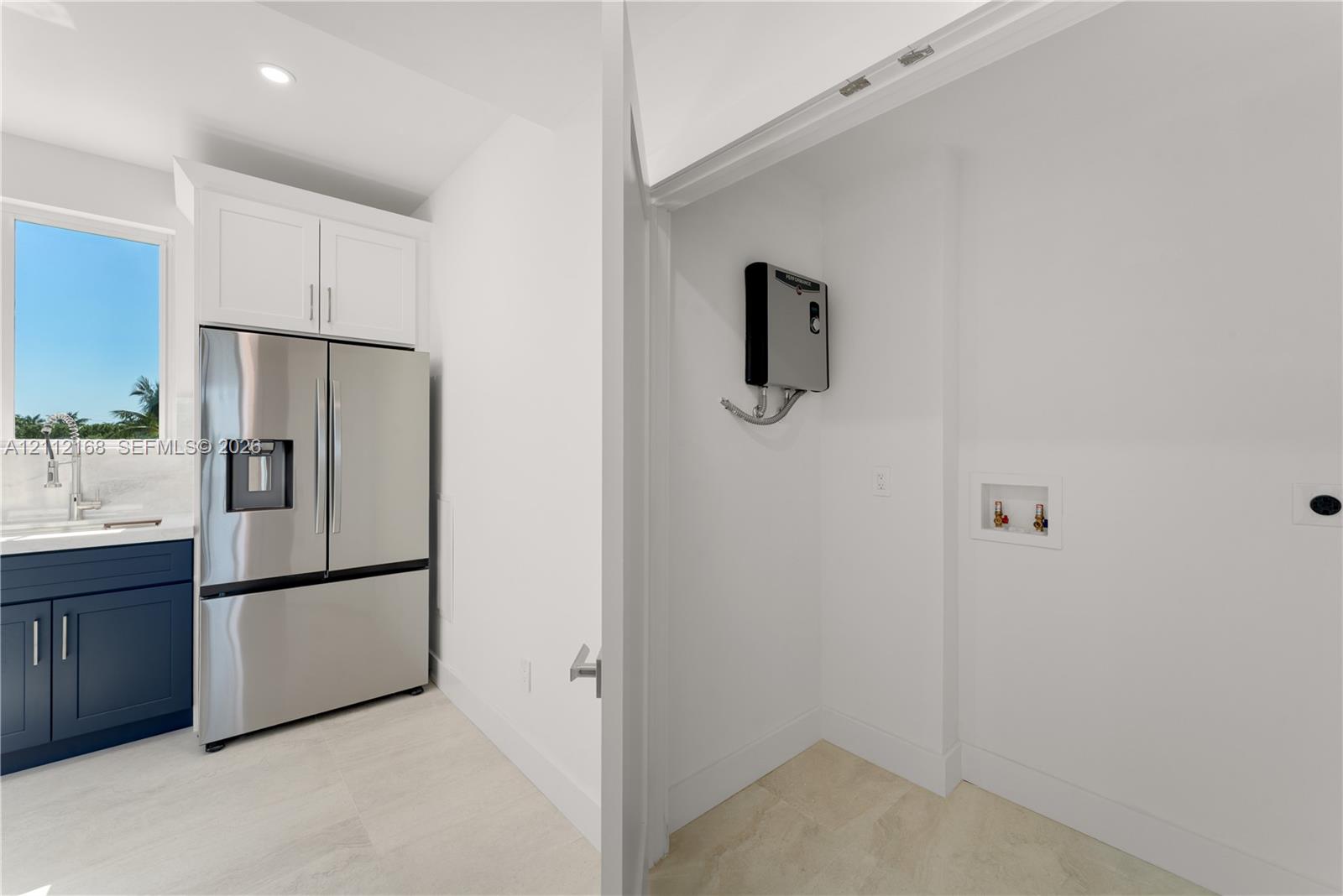 Stainless steel french-door refrigerator, dark navy cabinetry, white upper cabinetry, recessed lighting, and designated utility area with plumbing hookups
