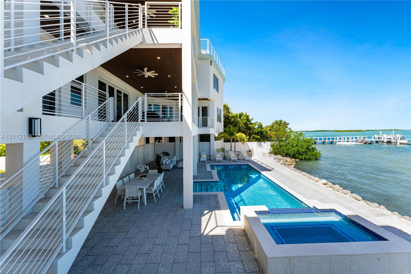 Multi-level exterior featuring a private swimming pool with integrated spa, paved pool deck, metal stair railings, and direct water access with a private dock
