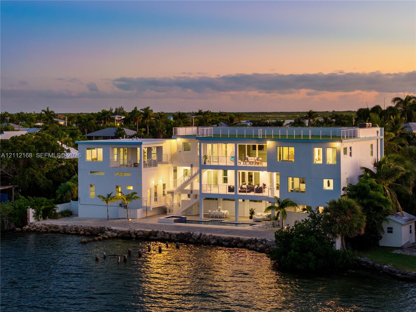 Waterfront residence featuring multi-level covered balconies, a rooftop deck with railing, a built-in pool, and a stone-lined bulkhead