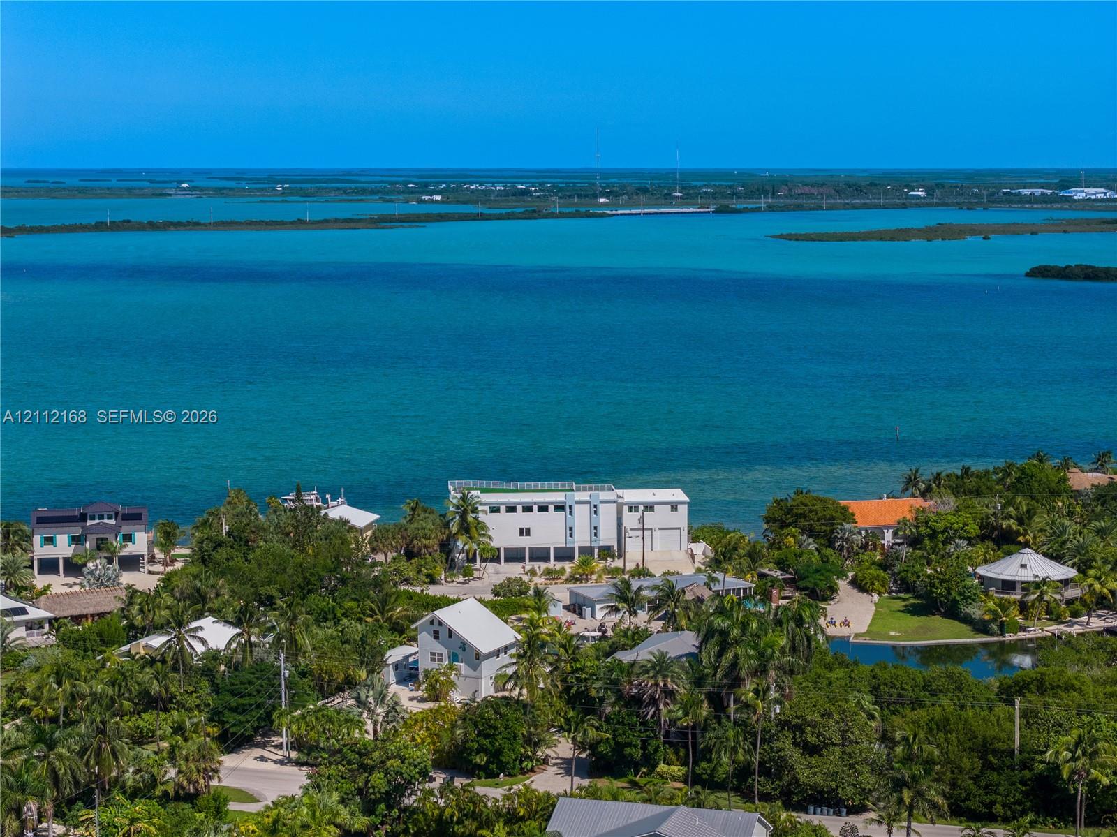 Waterfront property featuring direct coastal access, multi-level structural design, white exterior cladding, and expansive surrounding tropical vegetation