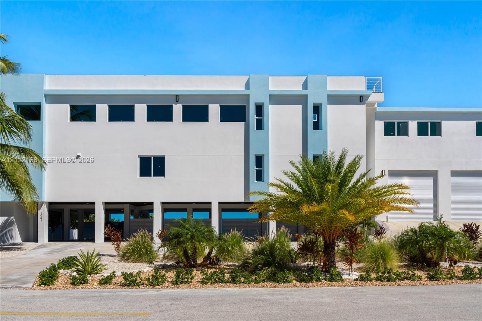 Multi-level exterior featuring smooth stucco finish, tiered flat roofline, oversized rectangular windows, ground-level covered parking, and attached multi-bay garage