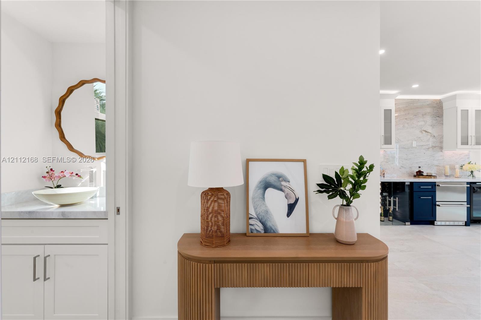 Custom vanity featuring a stone countertop, vessel sink, and scalloped-edge circular mirror, accented by cabinetry with flat-panel doors and recessed lighting