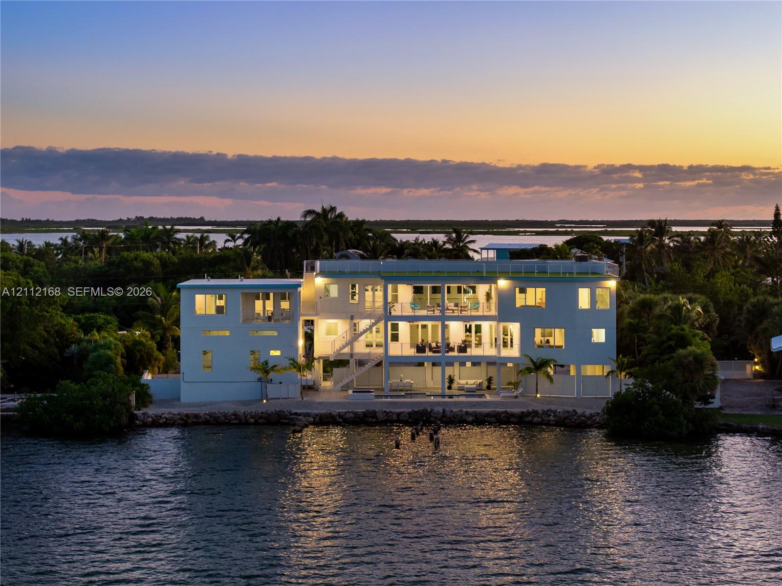 Waterfront residence featuring multi-level balconies, expansive glass windows, a flat roofline, and a private dock