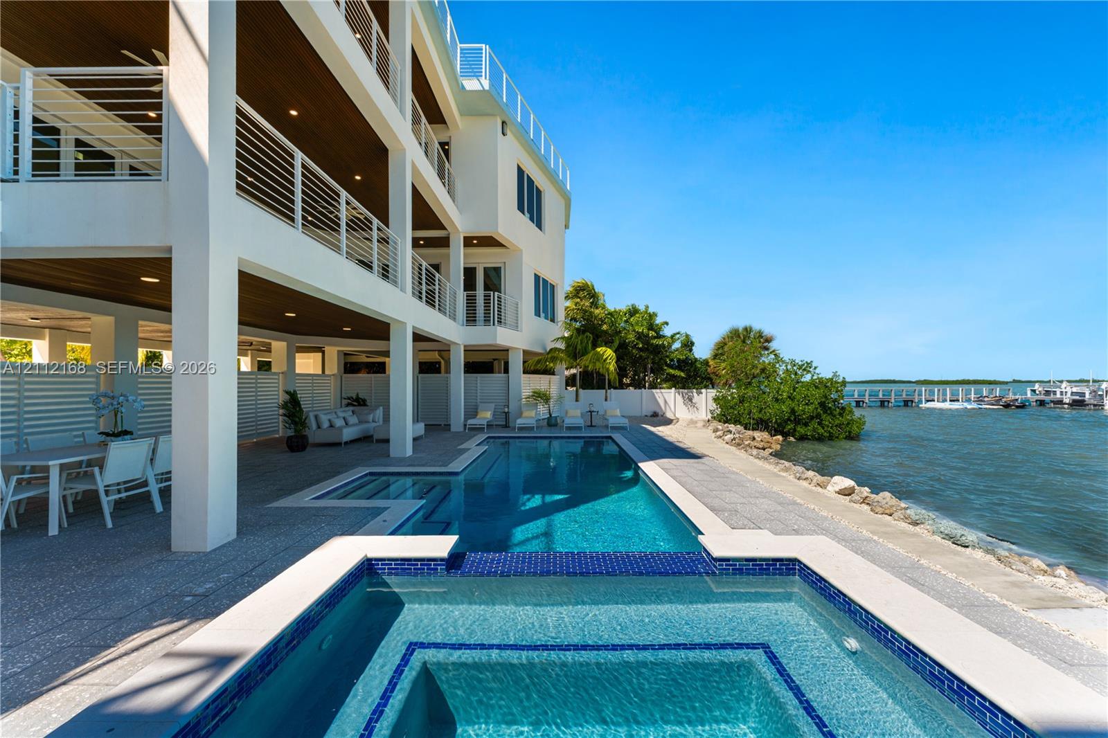 Multi-level exterior featuring tiered balconies with metal railings, a covered patio with recessed lighting, an integrated swimming pool and spa, and bulkhead waterfront access
