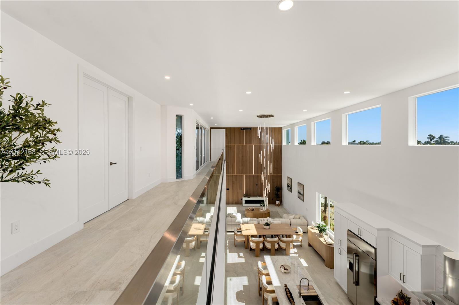 Elevated walkway featuring a sleek glass railing, wood-finish flooring, soaring ceilings, clerestory windows, and a multi-tiered modern chandelier