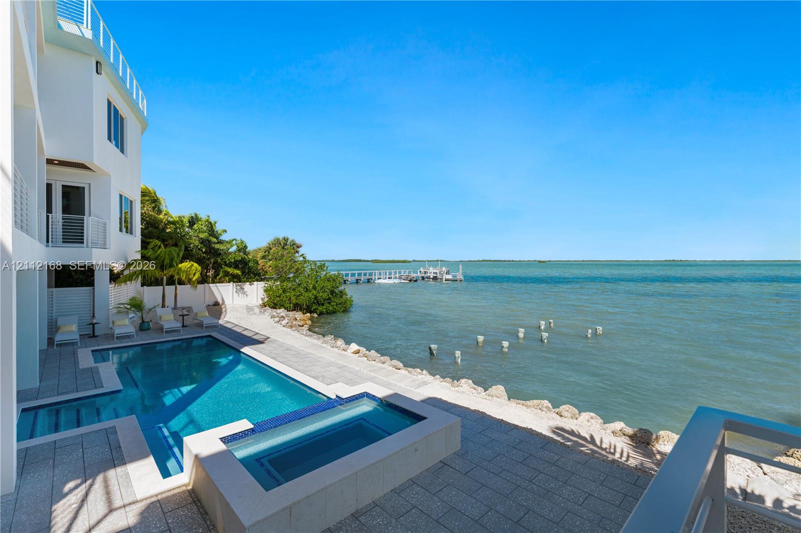 Waterfront property featuring an in-ground swimming pool, integrated spa, paved stone deck, and a private boat dock