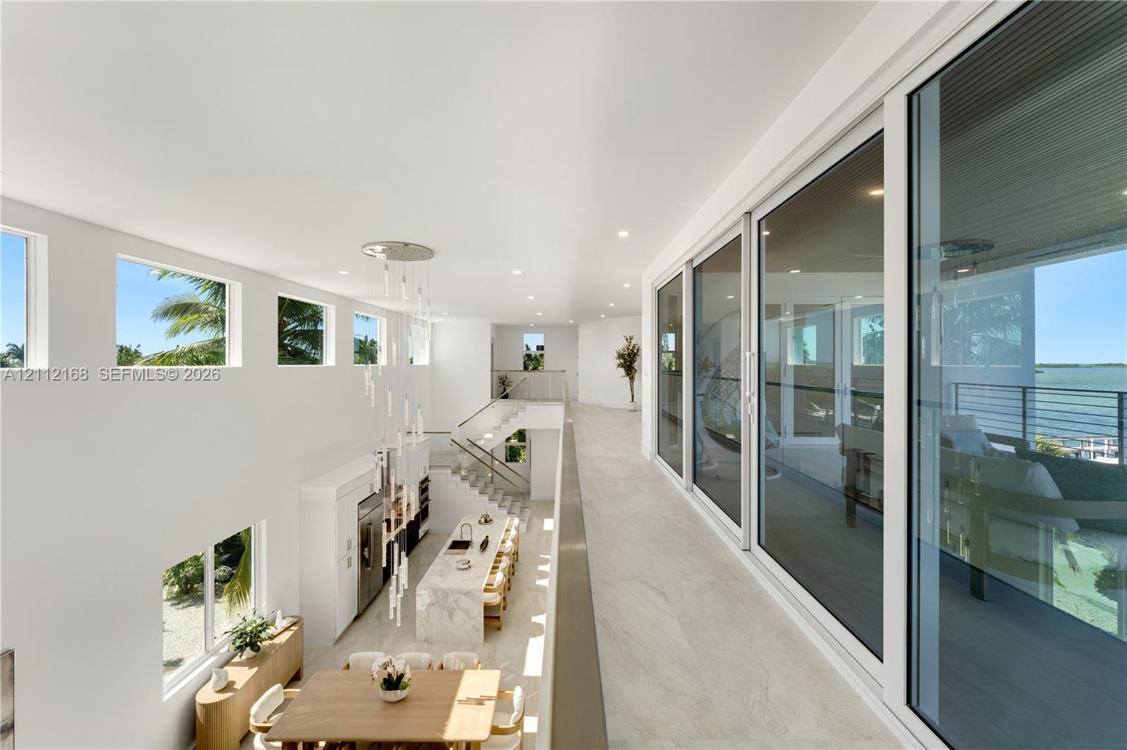 Open-concept upper level featuring large-format tile flooring, a multi-story glass pendant chandelier, expansive floor-to-ceiling sliding glass doors, and a metal-railing staircase