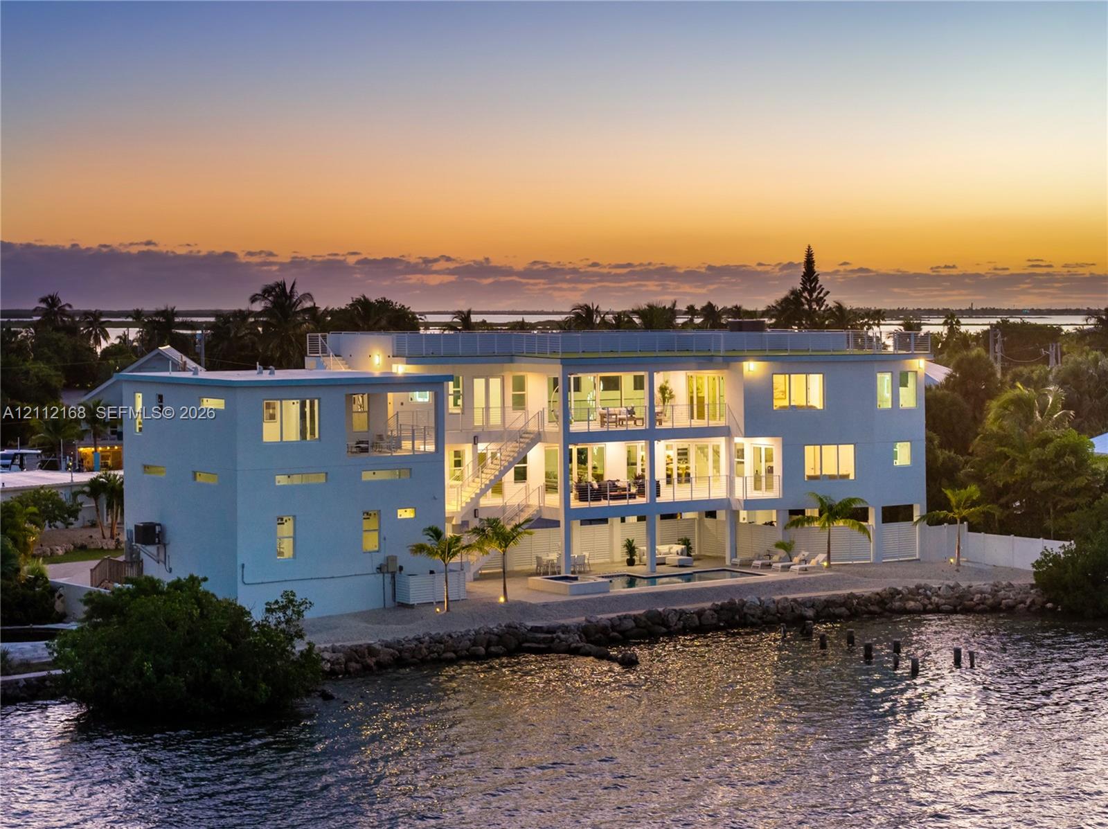 Waterfront multi-story residence featuring tiered balconies, a rooftop deck, exterior staircase, and a ground-level swimming pool