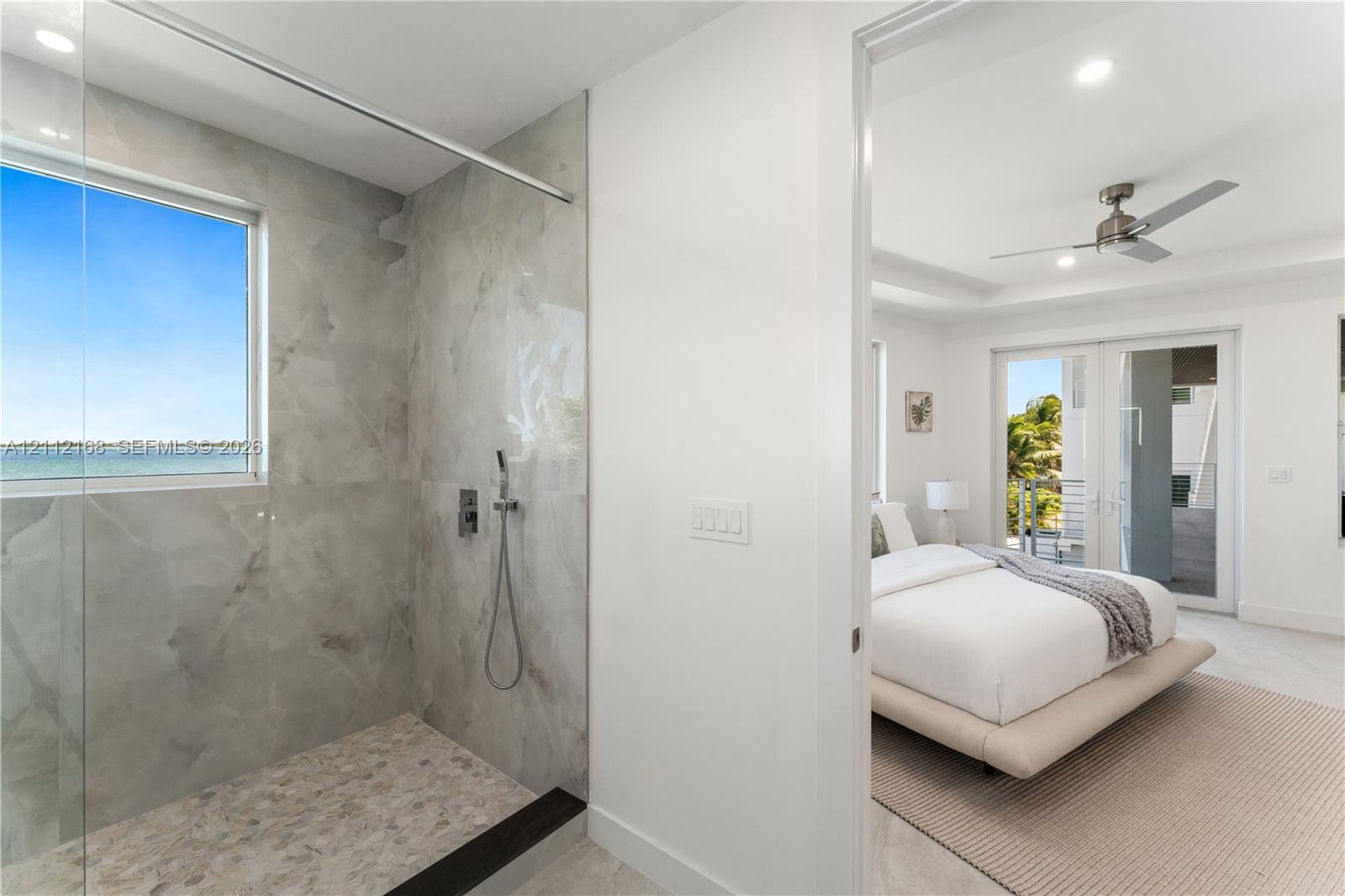 Walk-in shower featuring large-format tile surround, integrated window, handheld showerhead, pebble-finish flooring, and a frameless glass partition