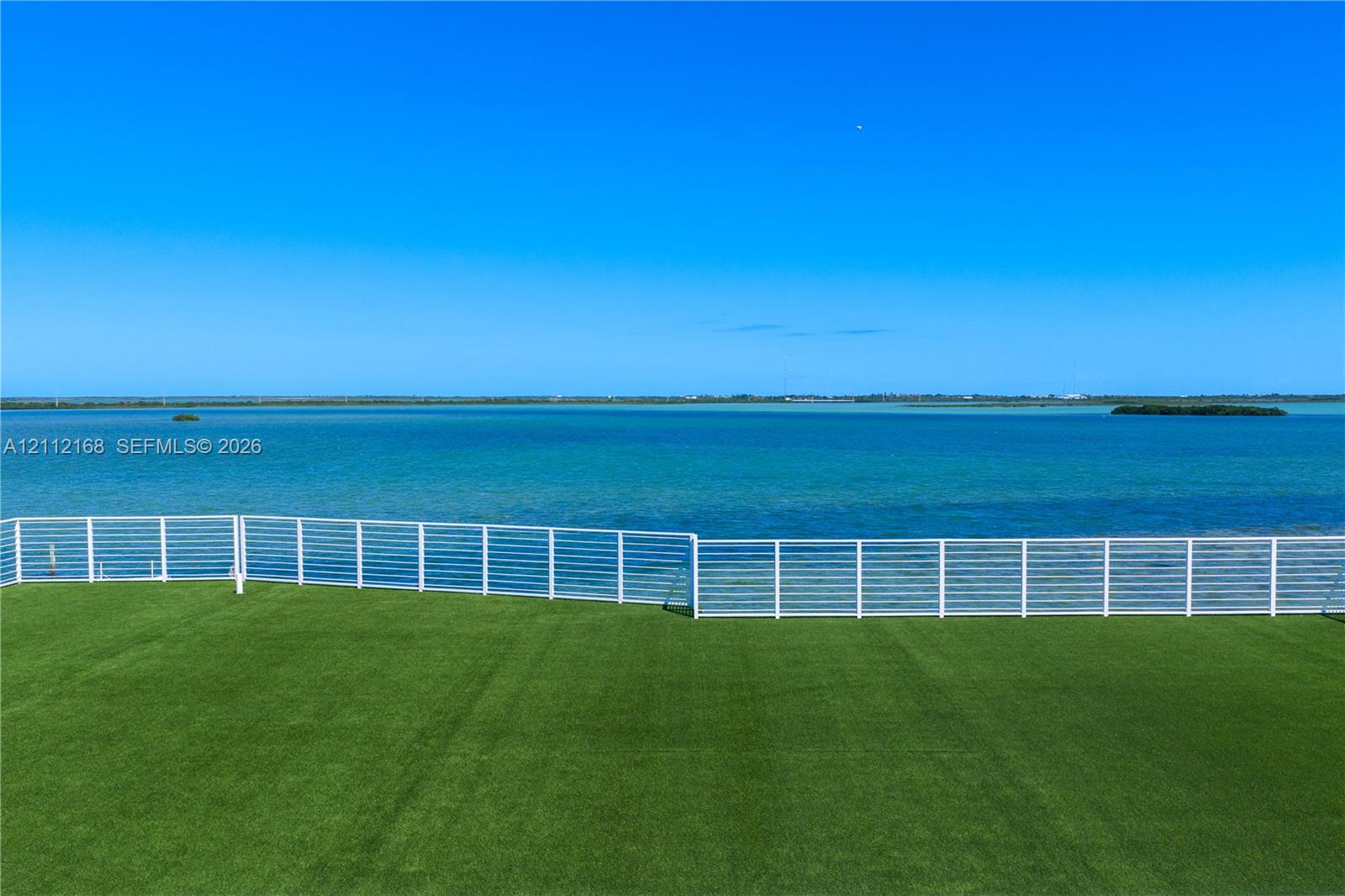 Outdoor space featuring synthetic turf and a white horizontal-slat metal railing, set against a waterfront backdrop
