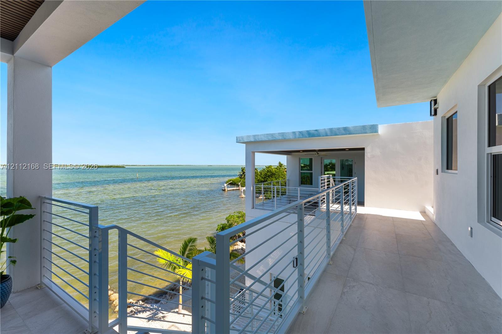 Covered waterfront balcony featuring large-format tile flooring, white metal cable railing, and a tongue-and-groove wood-finish ceiling