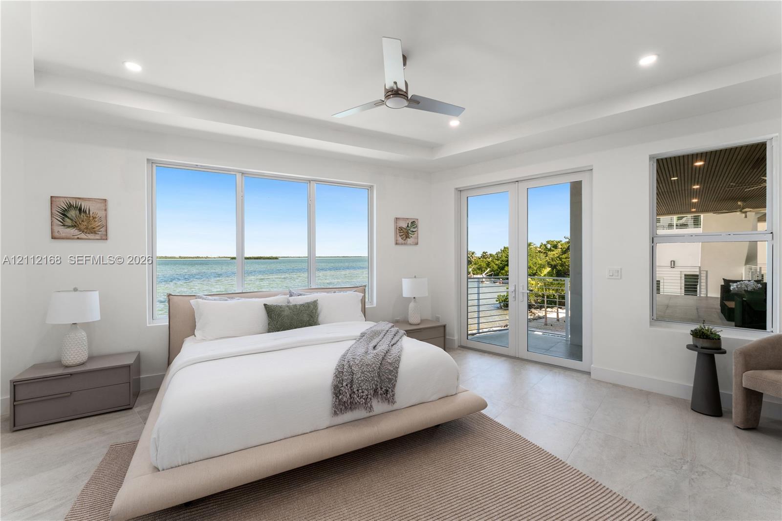 Tray ceiling with recessed lighting, floor-to-ceiling windows, modern ceiling fan, and glass-paneled double doors opening to a balcony