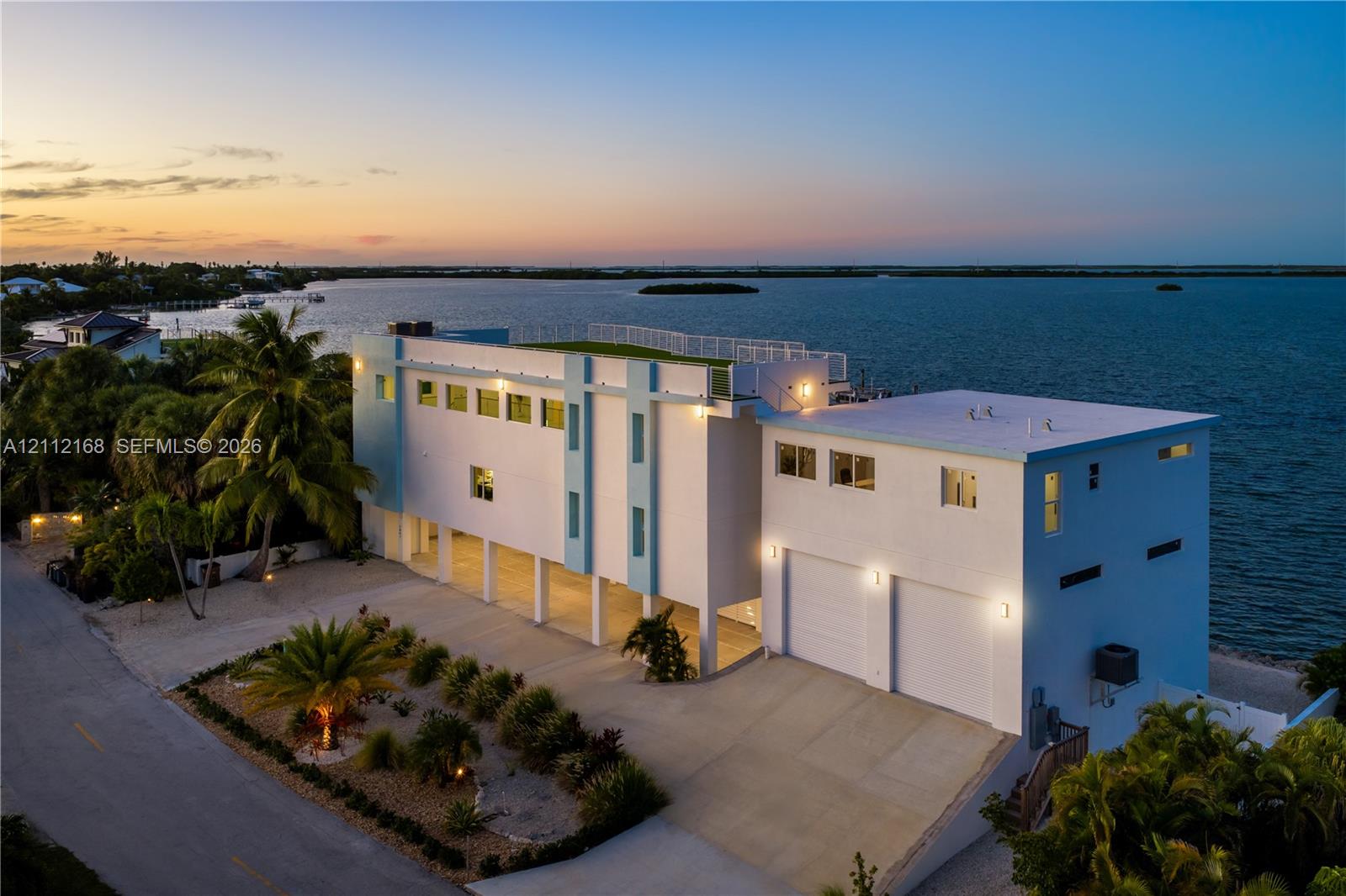Waterfront residence featuring a rooftop terrace, multi-level exterior structure, two-car garage, concrete driveway, and pilings foundation