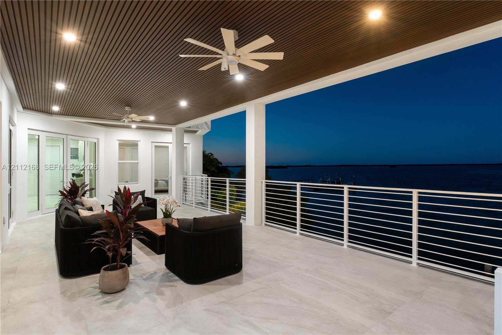 Covered terrace featuring large-format tile flooring, a slatted wood-finish ceiling with recessed lighting, dual ceiling fans, and a white horizontal rail system
