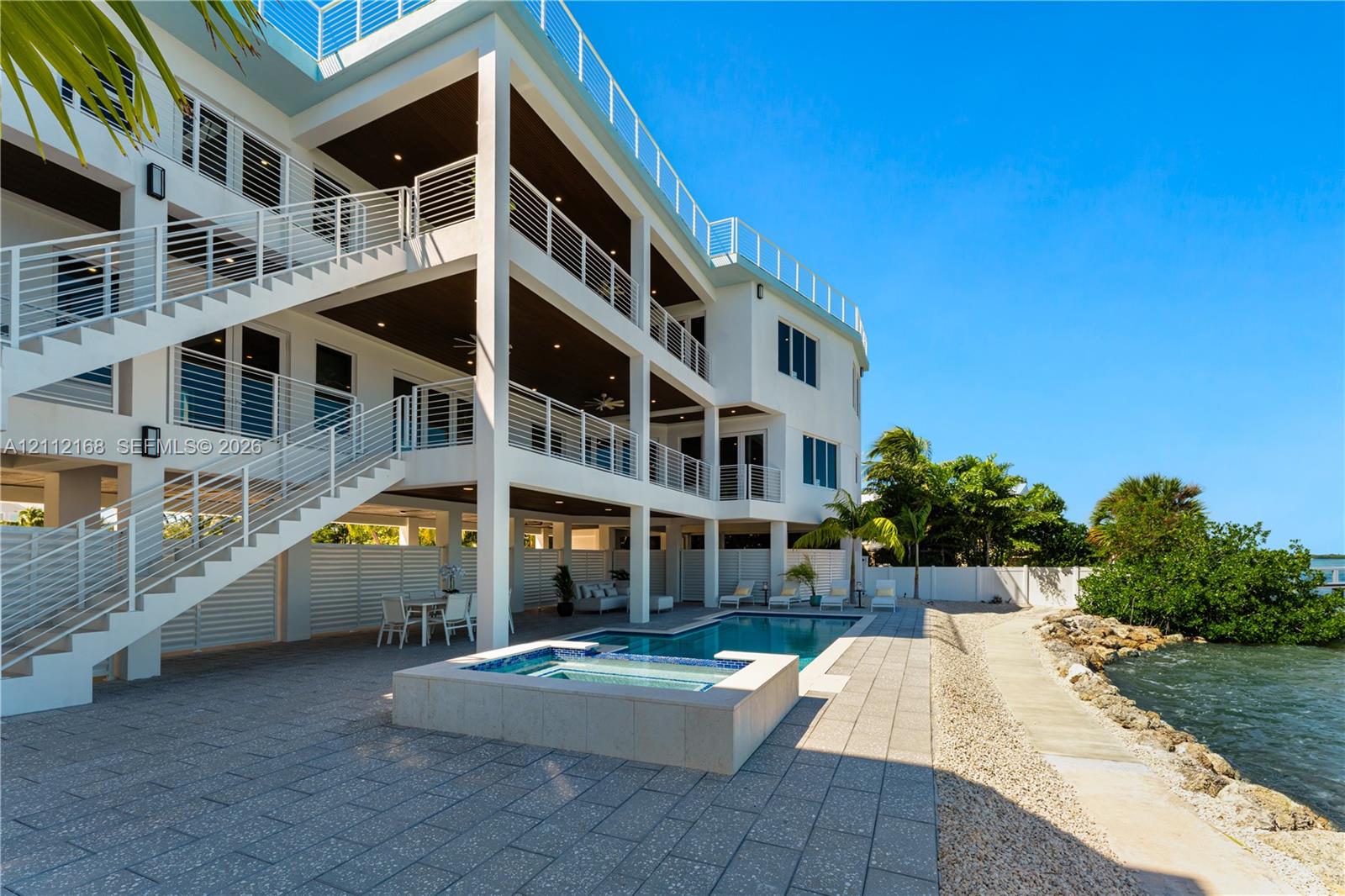 Multi-level residence featuring tiered outdoor balconies with horizontal railings, stone-tiled patio, in-ground swimming pool, and integrated spa