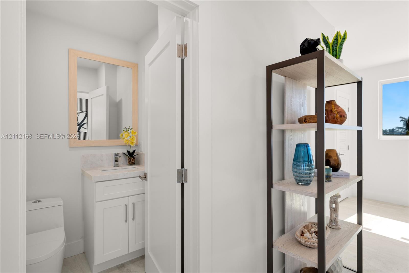 White cabinetry with stone-surfaced countertop, integrated under-mount sink, polished chrome faucet, and rectangular mirror with light wood-finish frame