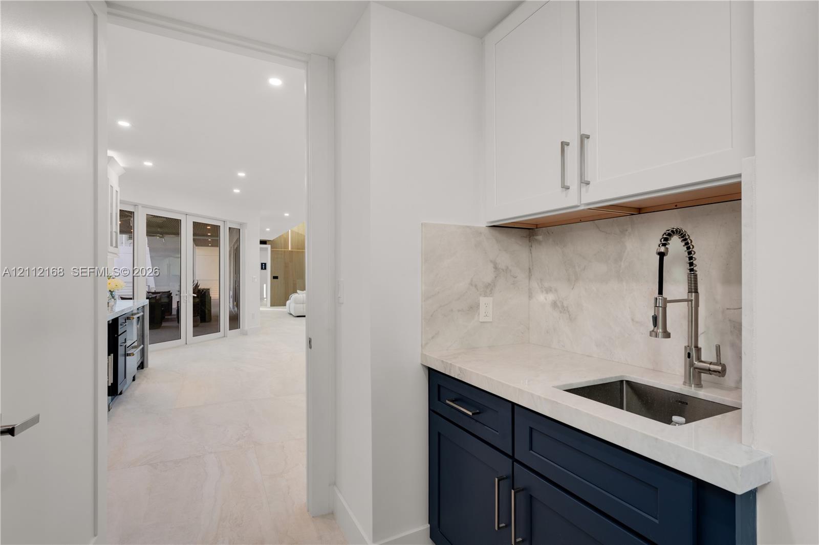 Wet bar featuring dark blue cabinetry, stone-finish countertop, coordinating backsplash, undermount stainless steel sink, and a gooseneck faucet
